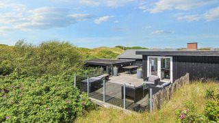 Terrasse der Seaside Charm Lodge in Rindby, umgeben von Dünen und Natur unter blauem Himmel.