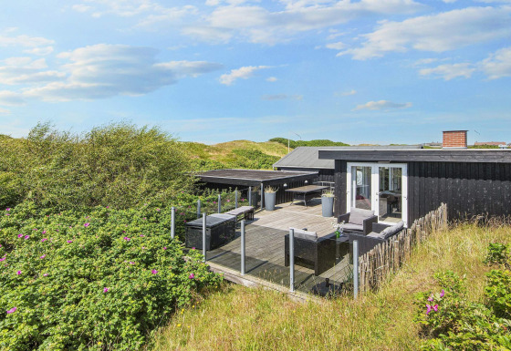 Terrasse der Seaside Charm Lodge in Rindby, umgeben von Dünen und Natur unter blauem Himmel.