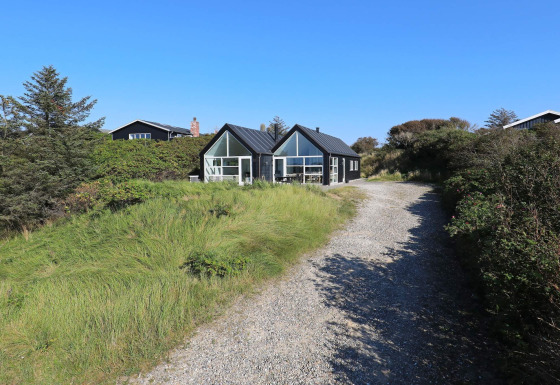Et feriehus til 6 personer i Blokhus med moderne sort træfacade, omgivet af grøn natur og blå himmel.