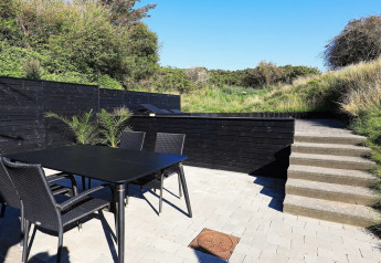 Terrasse extérieure du « gîte 6 personnes à Blokhus » au Danemark, avec table, chaises et verdure autour.