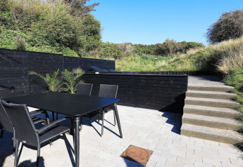 Terrasse extérieure du « gîte 6 personnes à Blokhus » au Danemark, avec table, chaises et verdure autour.
