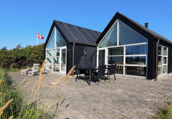 Maison de vacances moderne à Blokhus, Danemark, avec grandes baies vitrées, terrasse et drapeau danois.