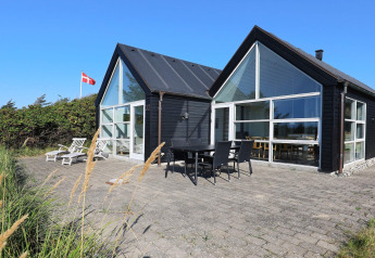 Modernes Ferienhaus in Blokhus, Dänemark, mit großer Terrasse, Sonnenliegen und dänischer Flagge.