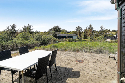 Udsigt fra terrasse med spisebord og fire stole ved feriehus i Blokhus, Danmark, omgivet af natur.
