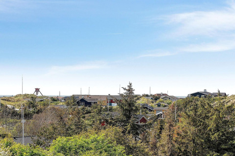 Blick von einem Ferienhaus in Blokhus, Dänemark, mit Hütten, grünen Bäumen und blauem Himmel.