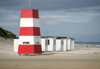Rood-witte strandtoren en vakantiehuisjes op zandstrand in Blokhus, Denemarken, onder bewolkte lucht.