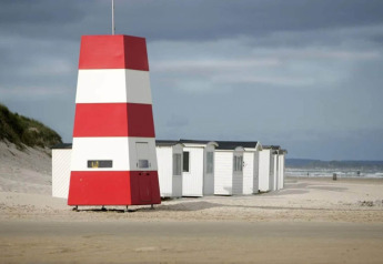 Rødt og hvidt strandtårn samt ferieboliger på sandstrand ved Blokhus, Danmark, under overskyet himmel.