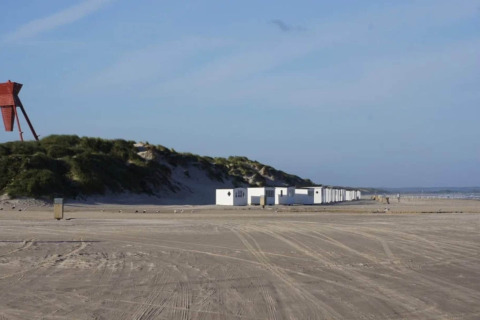 Strandzicht met duinen en witte vakantiehuisjes in Blokhus, Denemarken, op een zonnige dag.