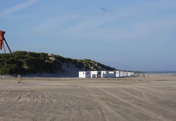 Strandzicht met duinen en witte vakantiehuisjes in Blokhus, Denemarken, op een zonnige dag.