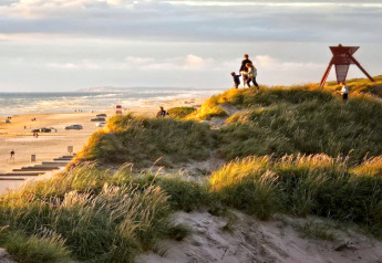 Des familles admirent le coucher du soleil sur les dunes d'une plage, près d'un lodge avec vue sur la mer.