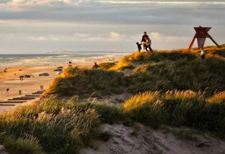Solnedgang ved klitterne på en dansk strand med familier, biler og udsigt over havet fra en lodge.