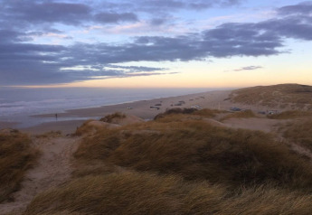 Blick von einer Lodge auf Dünen und Autos am Strand bei Sonnenuntergang und bewölktem Himmel.