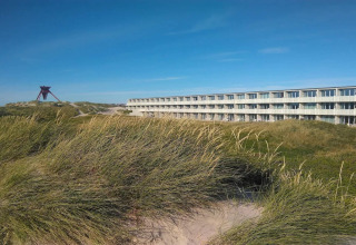 Blick auf die Dünen und das moderne '6-Personen-Ferienhaus in Blokhus', Dänemark, bei klarem Himmel.