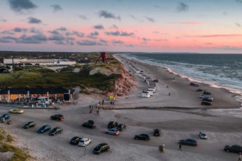 Solnedgangsudsigt over stranden ved Blokhus i Danmark med biler parkeret og hytter langs kysten.