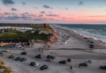Solnedgangsudsigt over stranden ved Blokhus i Danmark med biler parkeret og hytter langs kysten.