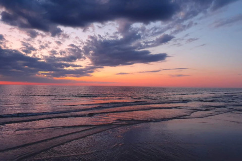 Solnedgang ved havet set fra en lodge, med bløde bølger og smukke farver på himlen og vandet.