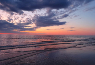 Solnedgang ved havet set fra en lodge, med bløde bølger og smukke farver på himlen og vandet.