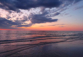 Tramonto sul mare visto da un lodge, onde leggere e colori vibranti del cielo riflessi sull'acqua.