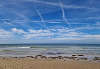 Vue depuis un lodge sur une plage paisible, ciel bleu clair, nuages fins et vagues douces de l’océan.