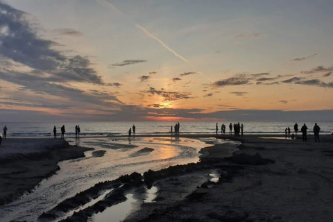 Solnedgang ved stranden i Blokhus, Danmark, med silhuetter af mennesker langs kysten.