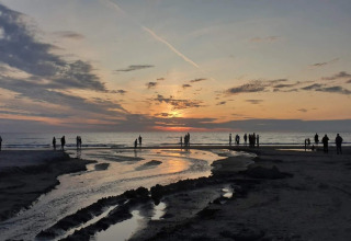 Zonsondergang op het strand van Blokhus, Denemarken, met mensen langs de kustlijn.