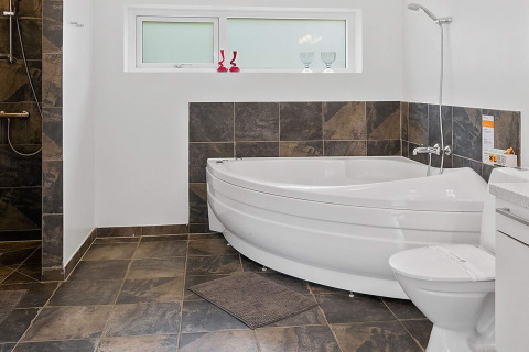 Moderne badkamer met hoekbad, douche, toilet en donkere tegels in een vakantiehuis in Blokhus, Denemarken.