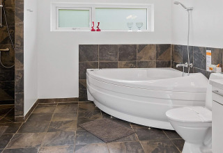 Modernes Badezimmer mit Eckbadewanne, Dusche, WC und dunklen Fliesen in einem Ferienhaus in Blokhus, Dänemark.