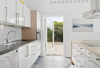Moderne keuken in vakantiehuis in Blokhus, Denemarken, met witte kasten en open deur naar de tuin.