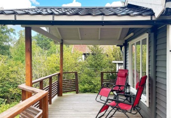Wooden deck with two red lounge chairs at a holiday home in Gränna, Sweden, surrounded by lush greenery.