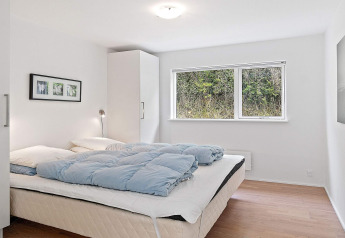 Dormitorio luminoso y minimalista con cama grande y ventana al bosque en casa vacacional en Blokhus, Dinamarca.