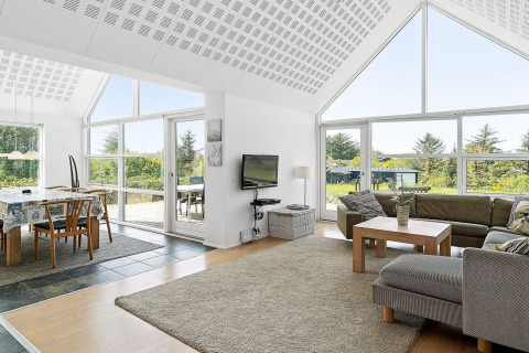 Helles Wohnzimmer mit großen Fenstern, Essbereich und gemütlichen Möbeln im Ferienhaus in Blokhus, Dänemark.