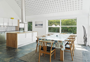 Moderne keuken en eetruimte in een vakantiehuis in Blokhus, Denemarken, met grote ramen en boszicht.