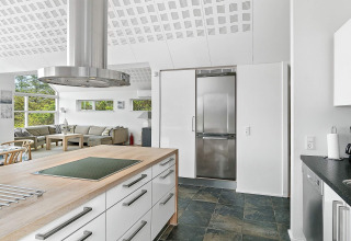 Moderne køkken og stue i et feriehus i Blokhus, Danmark, med store vinduer og stilfuld indretning.