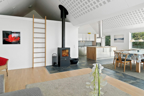 Modernes Ferienhaus in Blokhus, Dänemark, mit offener Küche, Holzofen, Esstisch und Leiter zum Dachboden.