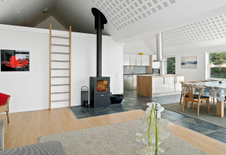 Modernes Ferienhaus in Blokhus, Dänemark, mit offener Küche, Holzofen, Esstisch und Leiter zum Dachboden.