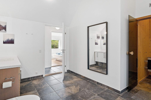Modernes Badezimmer in einem Ferienhaus in Blokhus, Dänemark, mit Fliesenboden, Spiegel und Sauna.