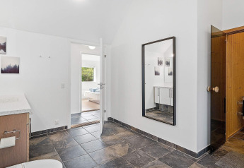 Modernes Badezimmer in einem Ferienhaus in Blokhus, Dänemark, mit Fliesenboden, Spiegel und Sauna.