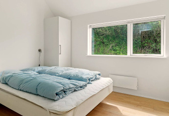 Chambre lumineuse avec lit double, couette bleue, armoire et grande fenêtre dans une maison de vacances à Blokhus.