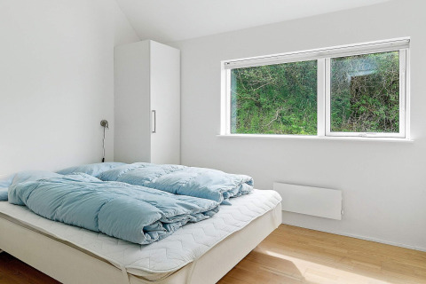 Lichte slaapkamer met een tweepersoonsbed, blauwe donsdeken, kast en groot raam in een vakantiehuis in Blokhus.