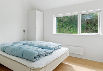 Heldere slaapkamer met tweepersoonsbed, blauw dekbed, kast en groot raam in een vakantiehuis in Blokhus.
