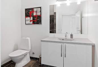 Bagno moderno nella casa vacanze per 6 persone a Blokhus, Danimarca, con arte astratta e grande specchio.