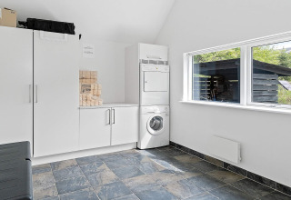 Moderner Hauswirtschaftsraum mit Waschmaschine, Trockner und Schränken in einem Ferienhaus in Blokhus, Dänemark.