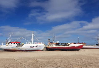 Vissersboten op het zandstrand onder een blauwe lucht, waarschijnlijk vlakbij een visserslodge.
