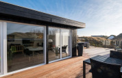 Große Holzterrasse bei der Lodge 'Seaside Charm in Rindby', Dänemark, mit Sitzbereich und Glasfassade.