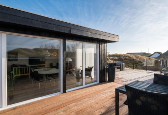 Große Holzterrasse bei der Lodge 'Seaside Charm in Rindby', Dänemark, mit Sitzbereich und Glasfassade.