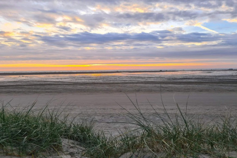 Sonnenuntergang am Strand, gesehen von einer Lodge mit Gras im Vordergrund und Wellen im Hintergrund.
