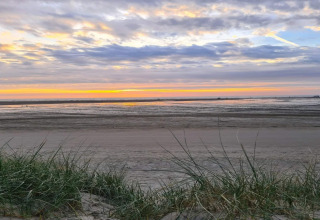 Sonnenuntergang am Strand, gesehen von einer Lodge mit Gras im Vordergrund und Wellen im Hintergrund.