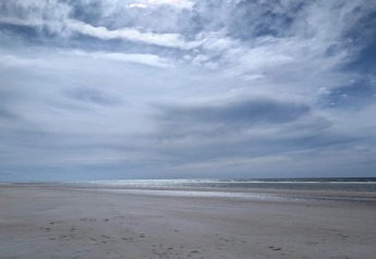 Ruhiger Strand mit bewölktem Himmel, fotografiert von einer Lodge am Meer an einem stillen Tag.