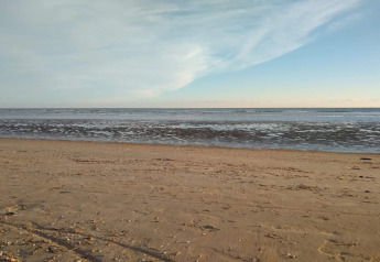 Foto eines ruhigen Strandes bei einer Lodge mit Sand und sanften Wellen unter blauem Himmel.