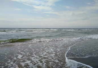 Aussicht auf das Meer bei einer Lodge mit sanften Wellen, die an einem leicht bewölkten Tag ankommen.